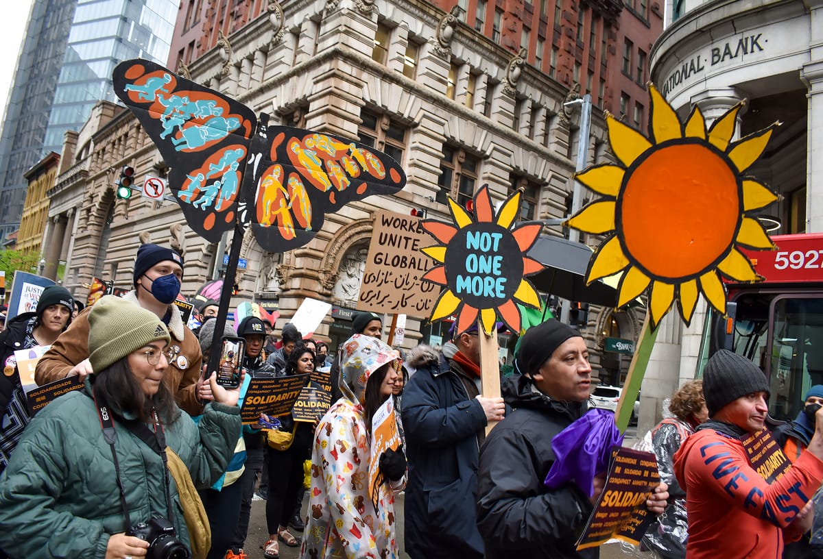 People walk together in a street for a protest holding colorful signs like a butterfly and flower